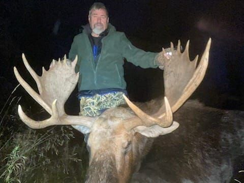 Hunter holding up the antlers of a harvested bull moose at night