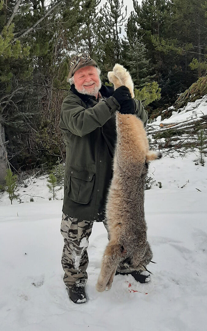 Hunter in the snow holding up a harvested lynx
